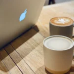Two coffee mugs and a laptop on a wooden desk in a coworking space — a quiet moment from my corporate to entrepreneur transition journey.