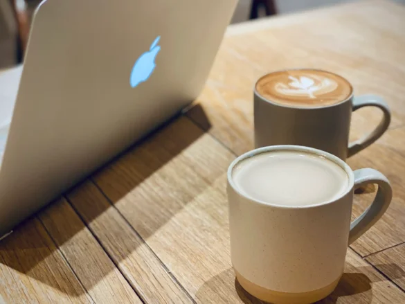 Two coffee mugs and a laptop on a wooden desk in a coworking space — a quiet moment from my corporate to entrepreneur transition journey.