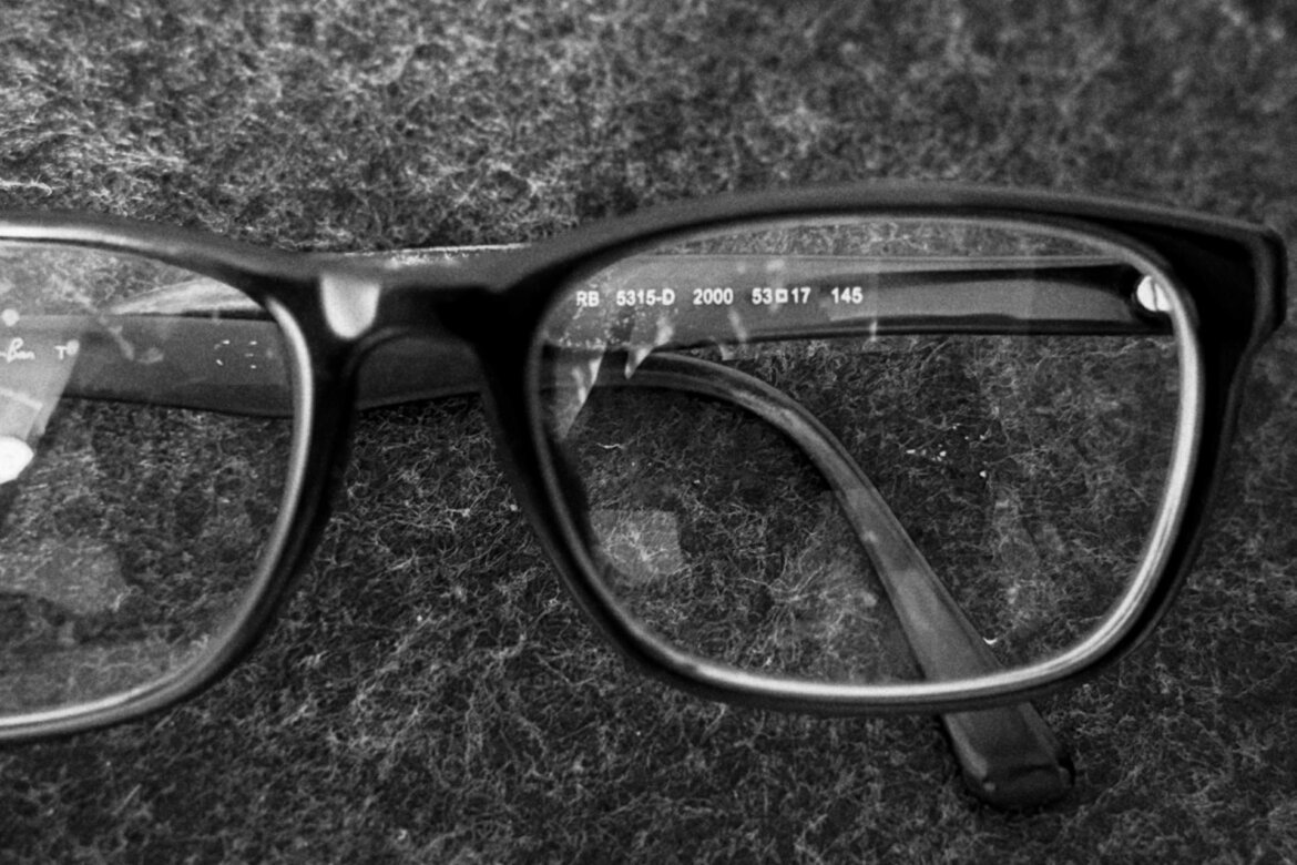 Black-framed rectangular eyeglasses resting on textured fabric, one lens showing printed frame details.