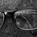 Black-framed rectangular eyeglasses resting on textured fabric, one lens showing printed frame details.