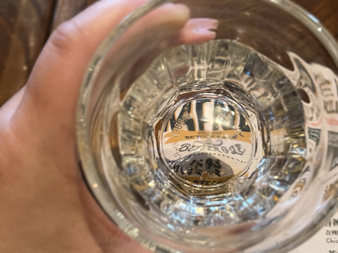 A hand holding a glass, with printed text distorted through its base.