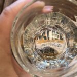 A hand holding a glass, with printed text distorted through its base.